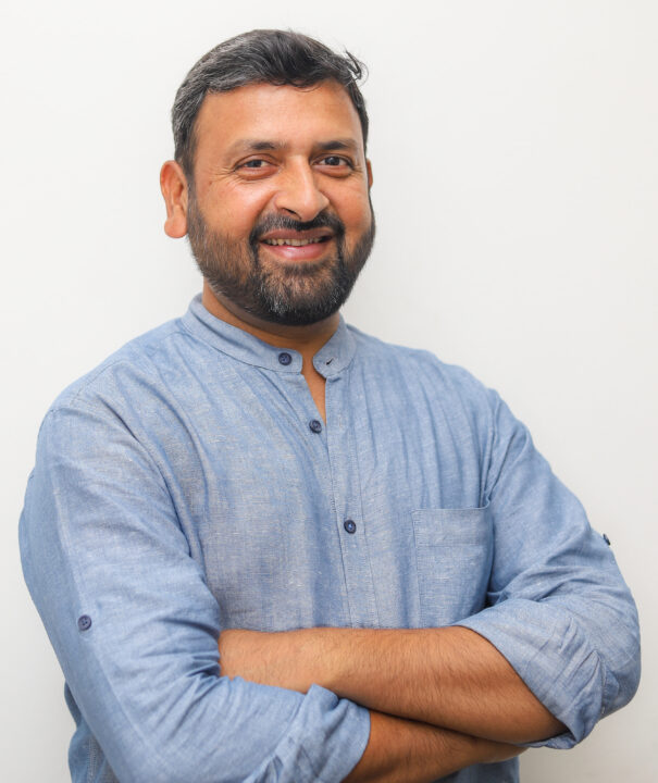 Man with beard and blue shirt smiling with arms crossed
