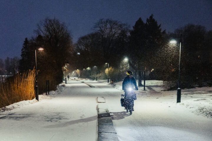 Cyclist riding through a snowy park at night with streetlights