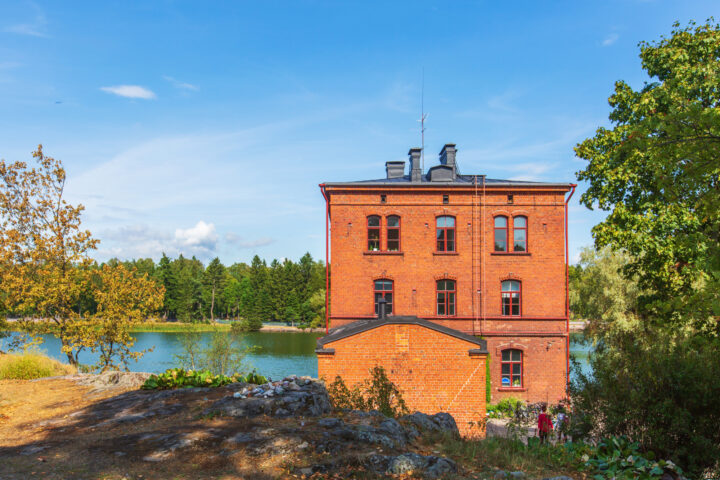 Red brick building by a lake in Finland, surrounded by trees in autumn