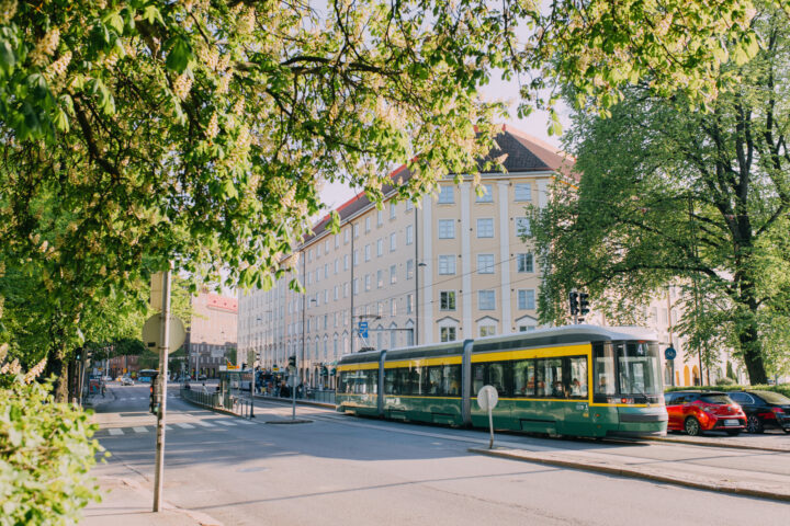Green and yellow tram on a city street lined with trees and buildings