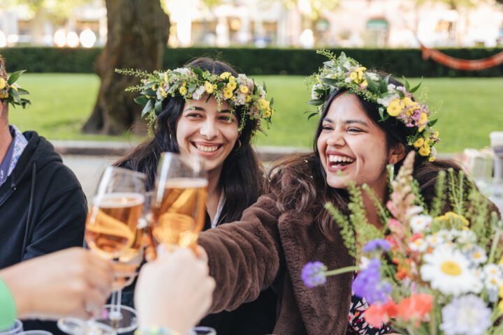 Two smiling women in flower crowns toast with champagne at an outdoor party.