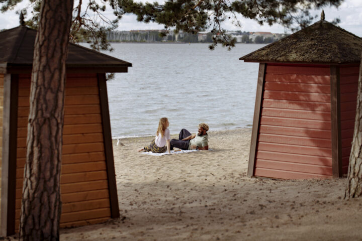 Couple relaxing on a sandy beach between two wooden changing rooms by the water