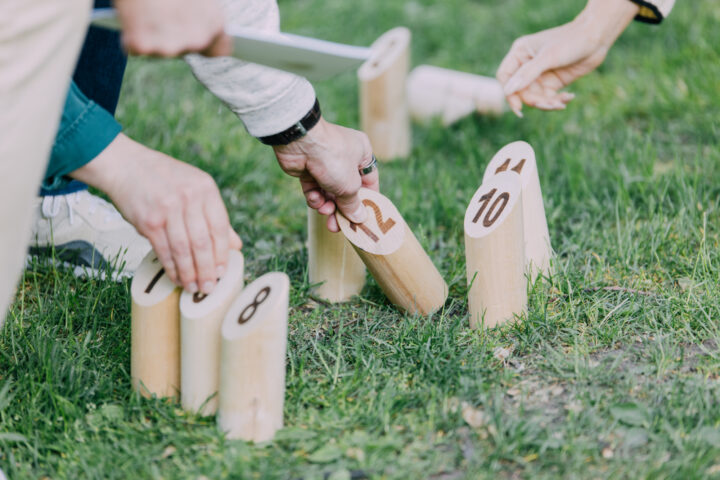 People playing Kubb, a lawn game with numbered wooden pins on grass.