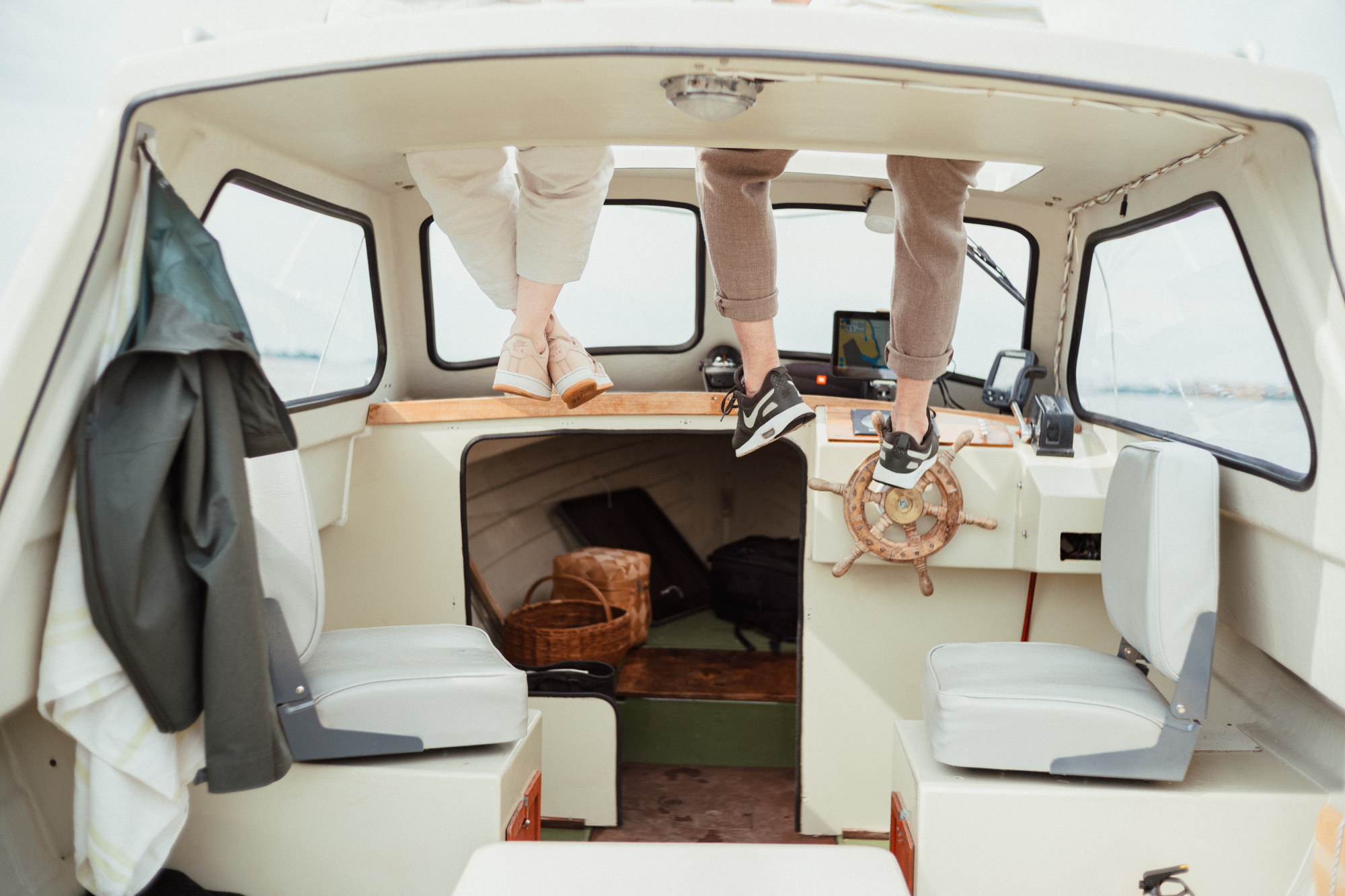 Inside boat with steering wheel and feet of people above dashboard