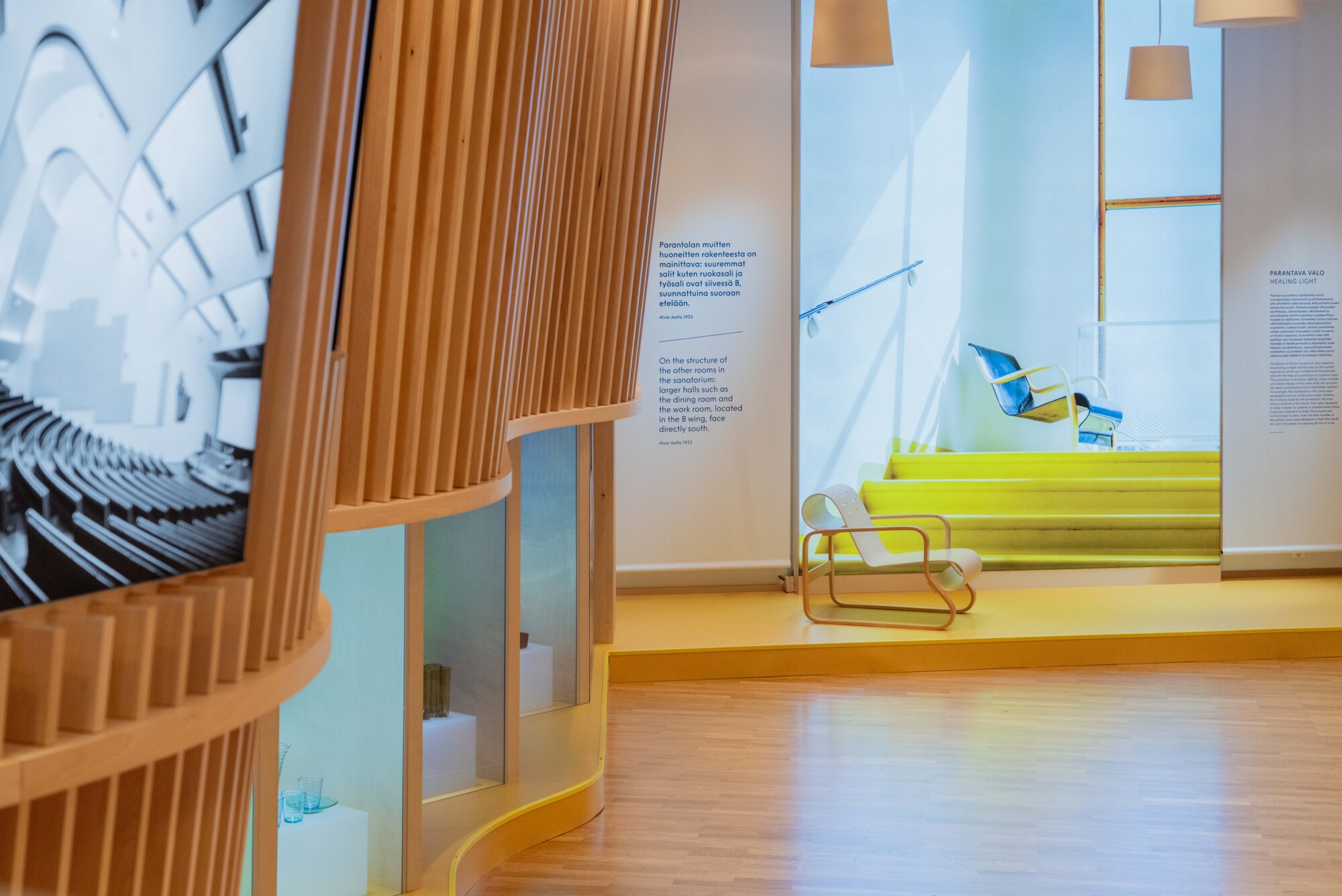 Museonäyttelyn sisätila, jossa on puulistoja, vitriinejä ja keltainen portaikko.