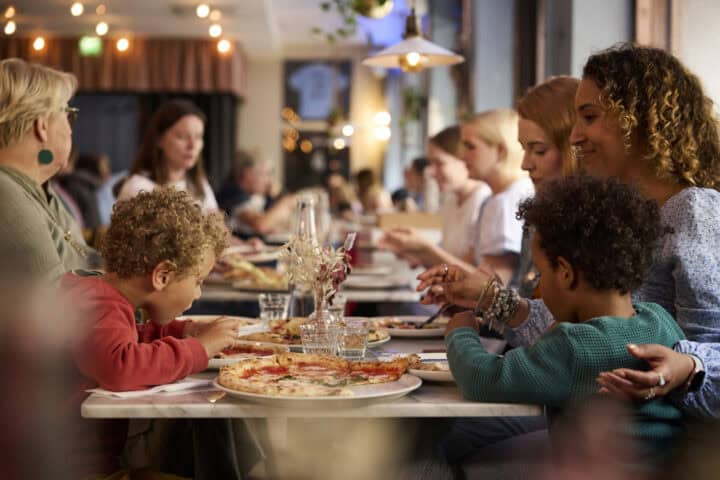Family enjoying pizza at a restaurant, with kids eating and adults talking.
