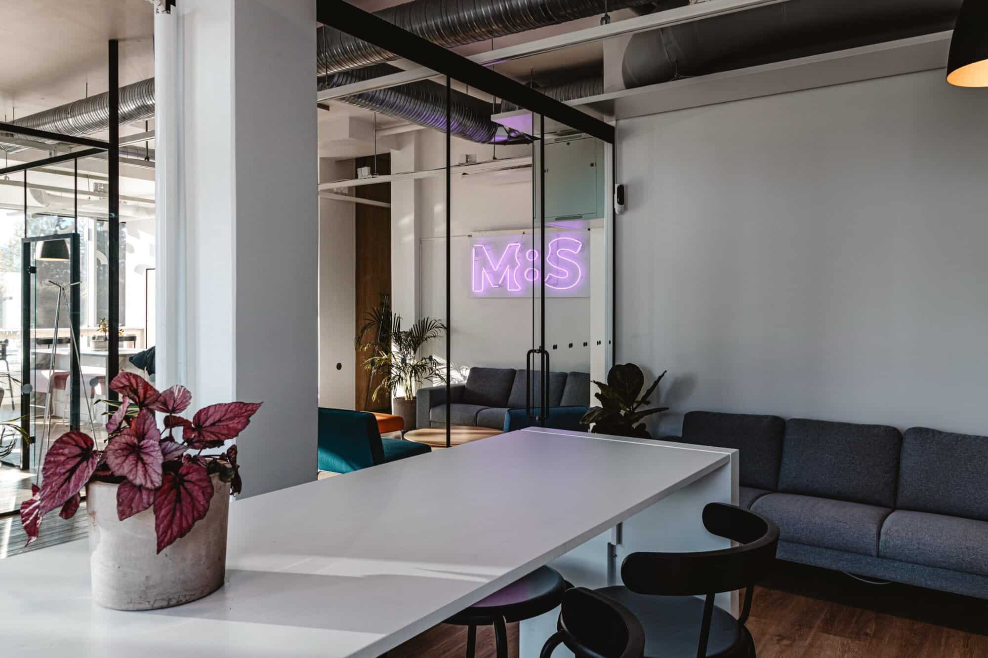 Loungen på M8S Hub & Studio med bord, soffor och en lila M8S-ljusskylt.
